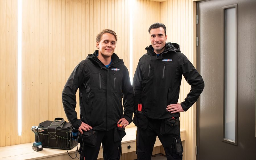 to elektrikere fra norgeseliten står utenfor en boligdør